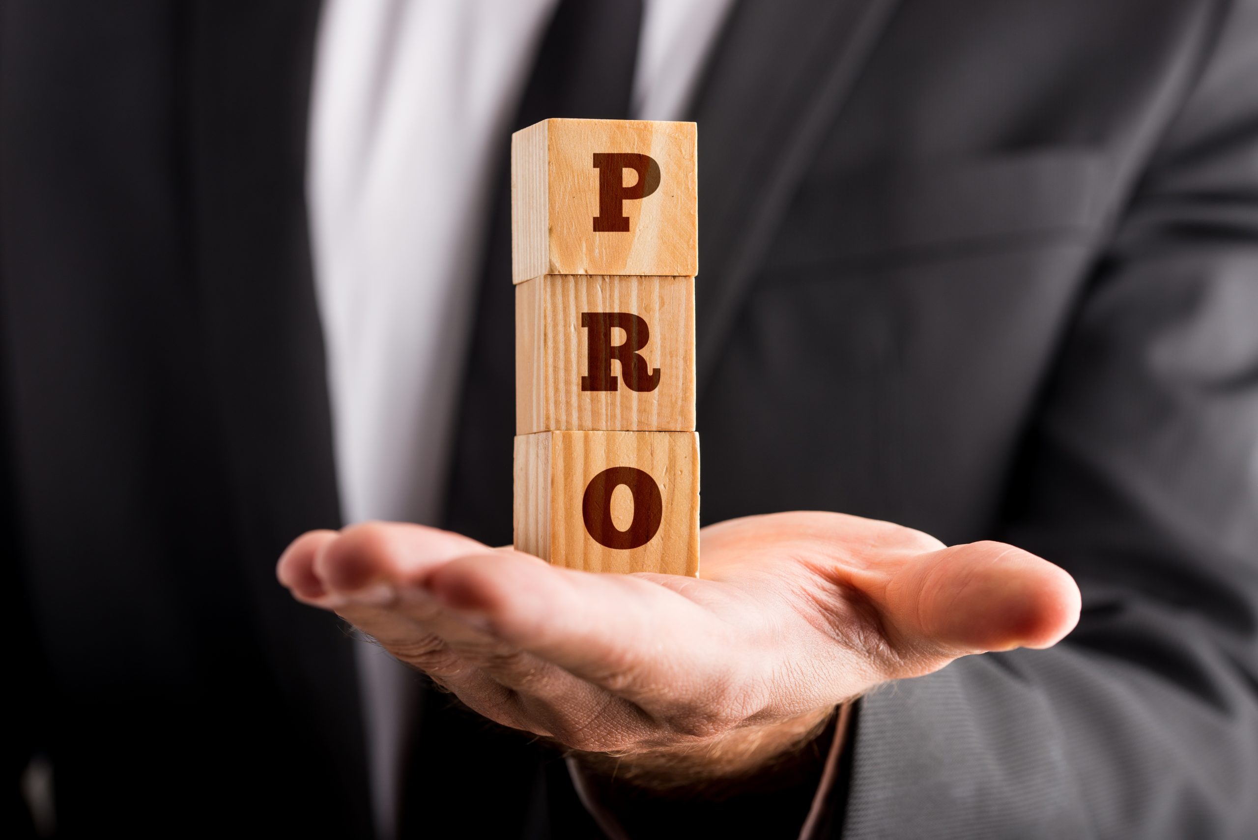 Businessman holding three wooden cubes stacked on the palm of his hand reading a PRO sign. Conceptual of professionalism and success.
